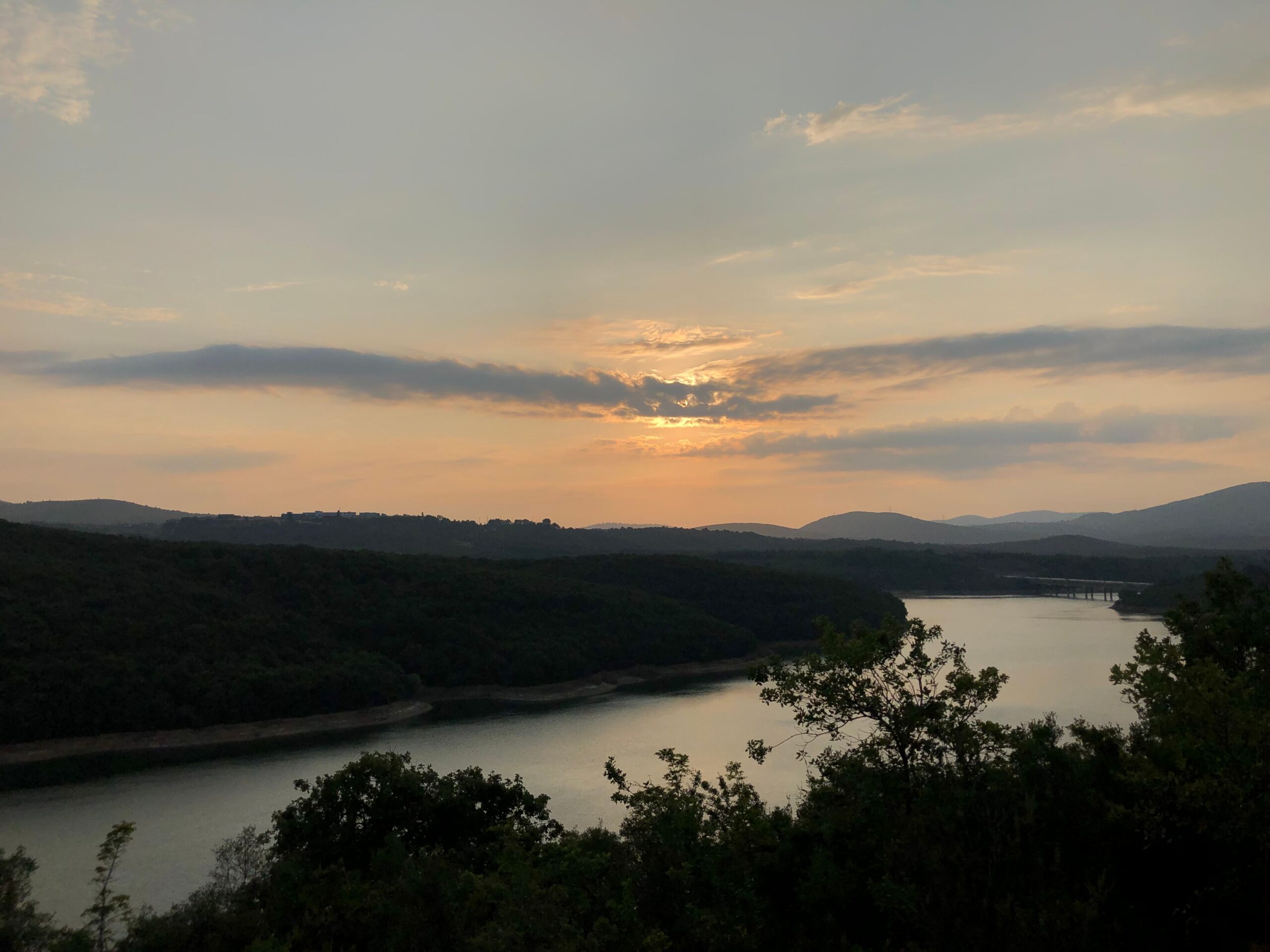 Beautiful sunset over a tranquil river surrounded by lush forests and hills.